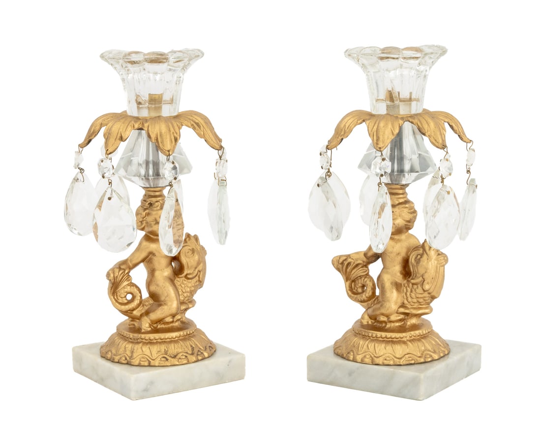 Hollywood Regency Gilt Metal Candlesticks, 2: Pair of Hollywood Regency Gilt Metal Figural Candlesticks, each with cherub atop a porpoise, molded glass flower form bobeche, and faceted tear drop prisms mounted on marble base, marked to underside.