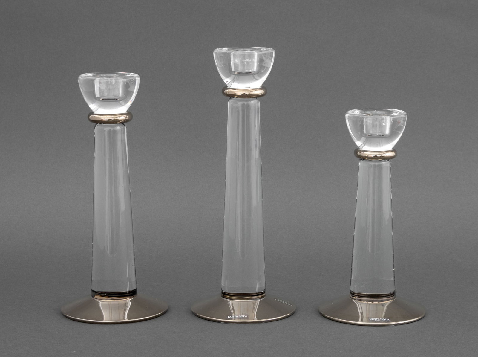 Ehner x Kosta Boda "Athena" Glass Candlesticks, 3: Group of Three Anna Ehner for Kosta Boda "Athena" Glass Graduated Candlesticks, with platinum accents, each with label to base and etch marked to underside. Largest: 10" H x 4" Diameter. Provenance: F