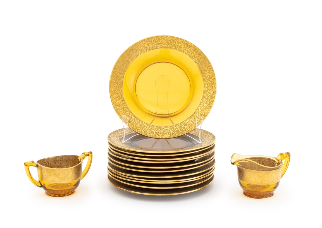 Gilt Encrusted Amber Glass Tableware, 14 Pcs.: Collection of Fourteen Gilt Encrusted Amber Glass Tableware Pieces, comprising: set of 12 dessert plates, a double handled cup, and a creamer jug. Plate: 8" Diameter x 1" H. Provenance: From a New Yor