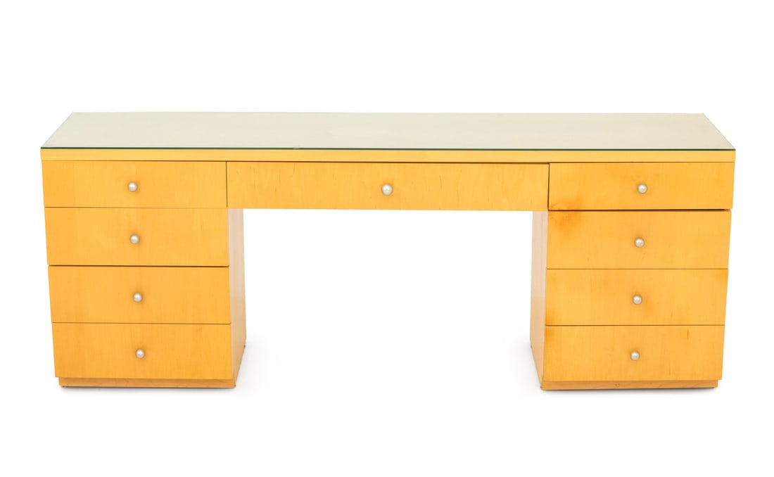 Art Deco Style Blonde Wood Writing Desk Vanity: Art Deco Style Blonde Wood Writing Desk, after Donald Deskey (American, 1894-1989), with glass top above central long drawer flanked by banks of four drawers. 29.75" H x 76.75" W x 19.25" D. Provenanc