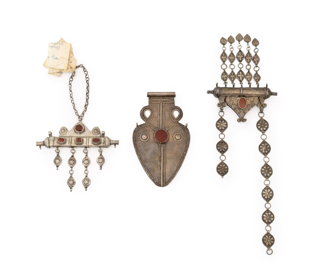 Turkmen Silver, Carnelian, Etc. Amulets, 3: Collection of Three Turkmen Amulets, comprising: an Asyk heart form silver pendant with red glass cabochon and two tumar pendants, one silver with carnelian cabochon and one silver-tone with three car