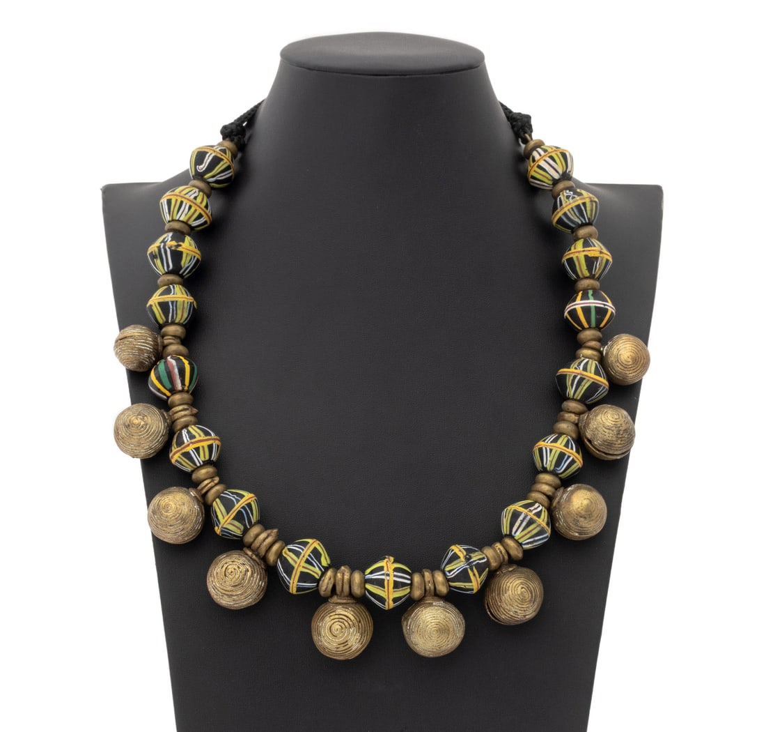 Irena Corwin Glass African Trade Bead Necklace: Irena Corwin (American, XX) Venetian Glass African Trade Bead Necklace, comprising of "King" beads and African Baule brass bell pendants. 40" L x 1.5" W. Provenance: From the Estate of Jewelry Designe