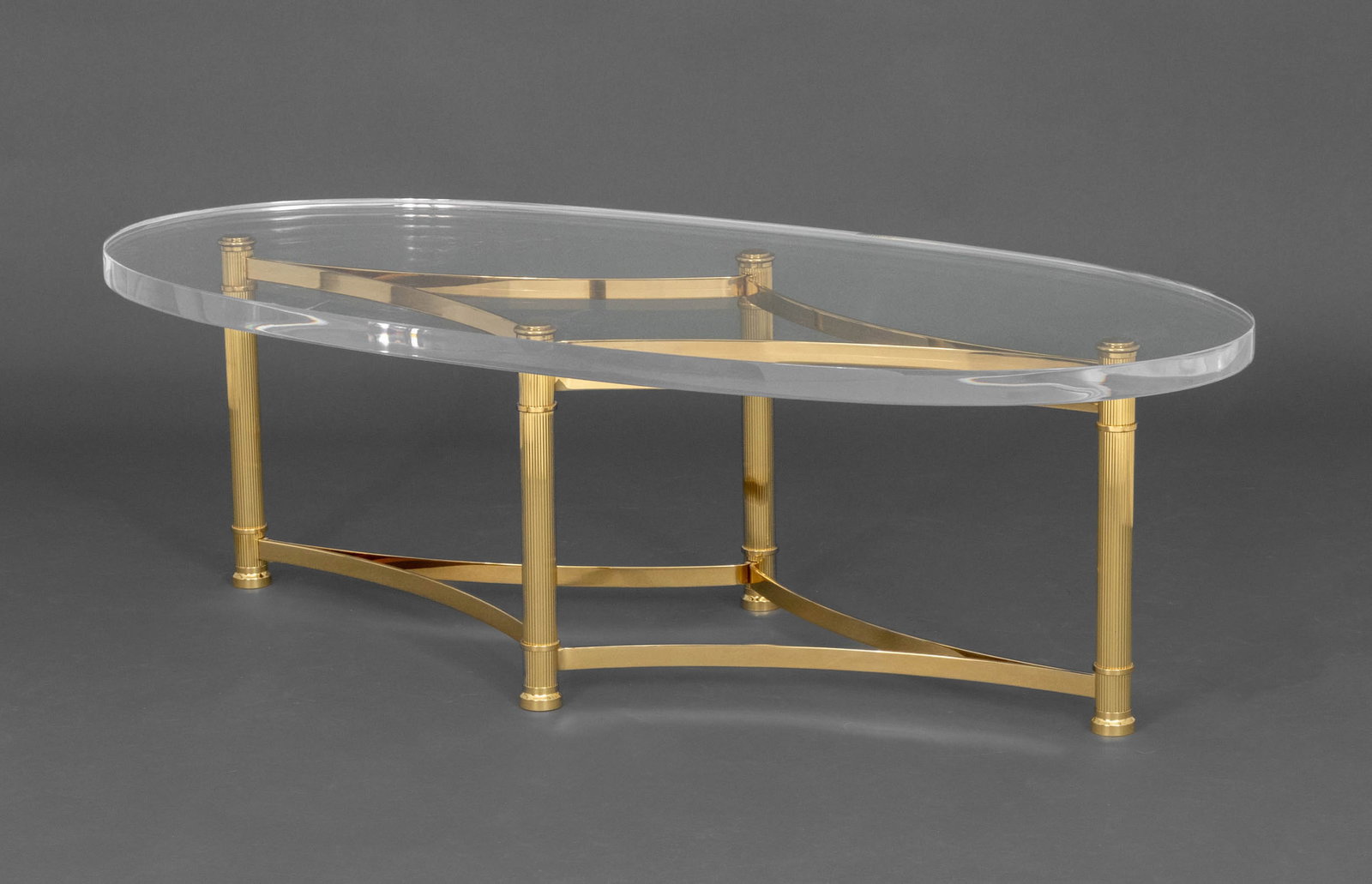 Modern Brass and Acrylic Oval Coffee Table: Modern Brass and Acrylic Oval Coffee Table, the base with four fluted columns conjoined by diamond form stretcher. 17" H x 55.5" W x 26.75" D. Provenance: From a 500 Park Avenue Estate. Keywords: Mode