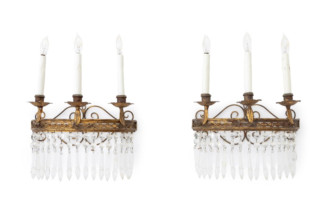 French Empire Style Gilt Iron Wall Sconces, Pair: Pair of French Empire Style Gilt Wrought Iron Three-Branch Wall Sconces, each with pierced scroll form back plate and drop crystal prisms. 15" H x 11" W x 5.25" D. Provenance: From a Connecticut Estat