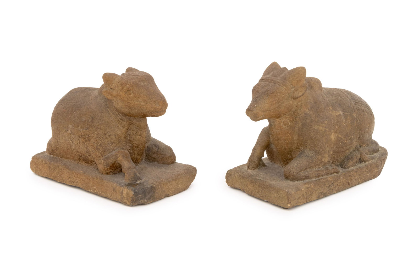 Indian Carved Sandstone Nandi Sculptures, Pair: Pair of Indian Carved Sandstone Nandi Sculptures, each cow reclining and outfitted with saddle, bridle, and headpiece atop rectangular base. 8" H x 11" W x 6" D. Provenance: From a New York City Colle