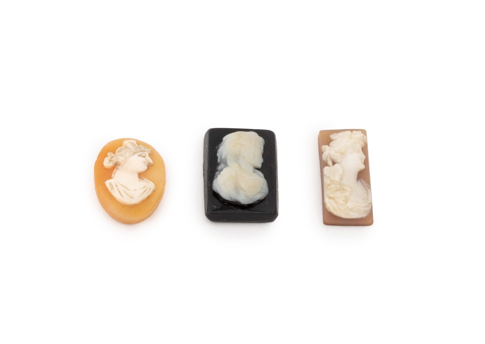 Female Silhouette Carved Cameo Cabochons, 3: Collection of Three Female Silhouette Carved Cameo Cabochons, two on an orange shell ground and one on a black ground. Largest approx.: 0.75" L x 0.5" W. Provenance: From a New York City Collection. K
