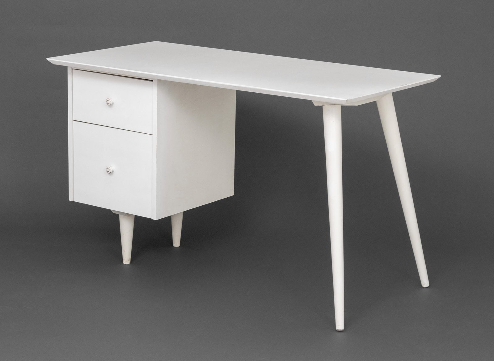 Paul McCobb Style White Painted Desk: Paul McCobb Style White Painted Desk, the two drawers with gilt porcelain pulls above tapered flaring legs. 29.25" H x 48" W x 24" D. Provenance: From an East 79th Street Estate. Keywords: Vintage Fur