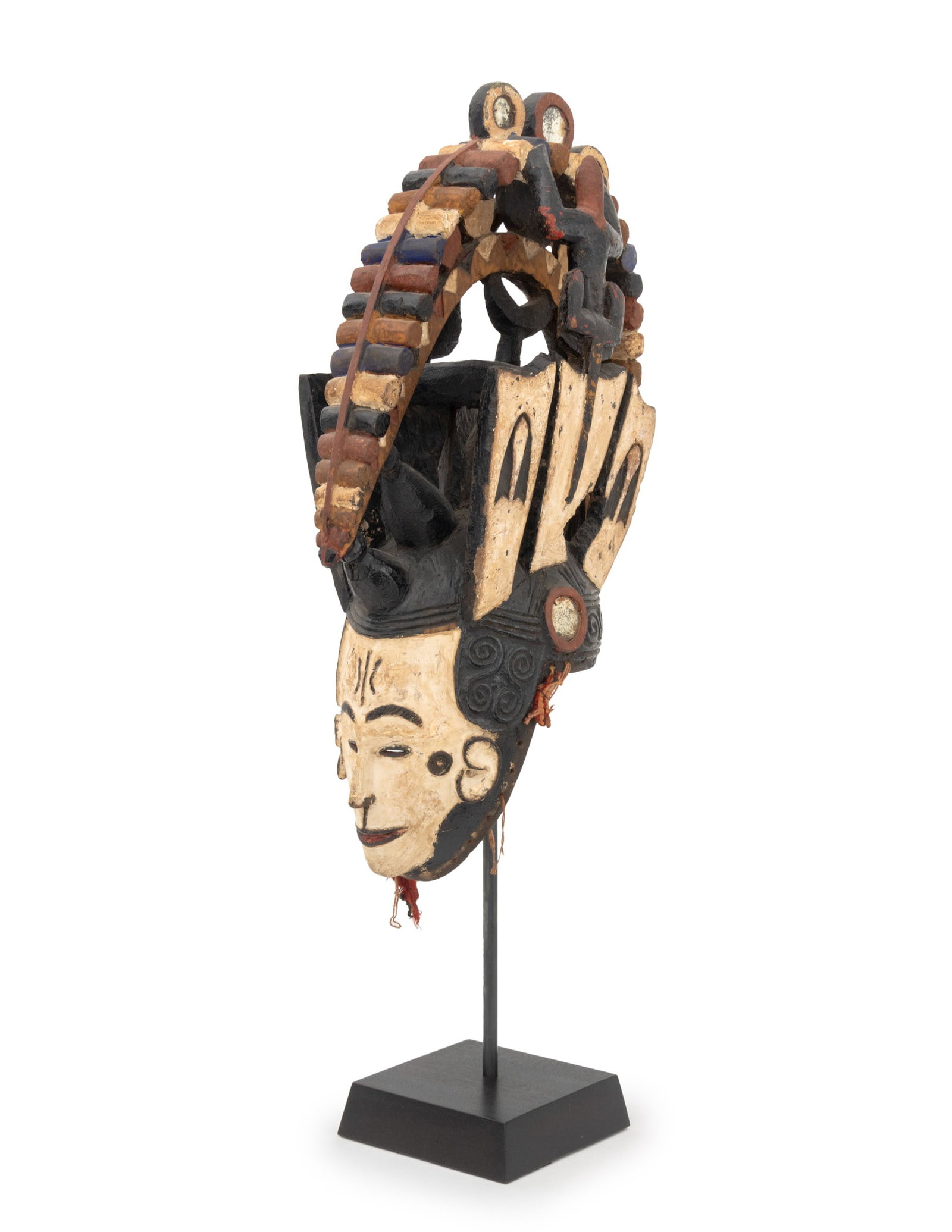 African Igbo Agbogho Mmwo Helmet Mask: African Igbo Agbogho Mmwo Helmet Mask, Nigeria, polychrome painted and carved wood with mirrored glass elements, with ebonized wood stand. Overall: 34" H x 8" W x 14" D. Provenance: Roger Lefevre, Bru