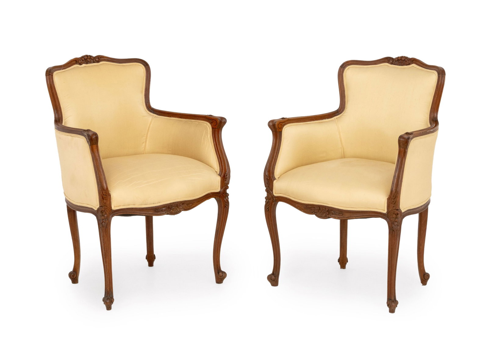 Louis XV Style Upholstered Walnut Bergeres, Pair: Pair of Louis XV Style Upholstered Walnut Bergeres, with cream fabric upholstery and floral motif carvings. 35" H x 25" W x 22" D; seat: 20" H. Provenance: From the Estate of Joseph Lawrence Gardella.