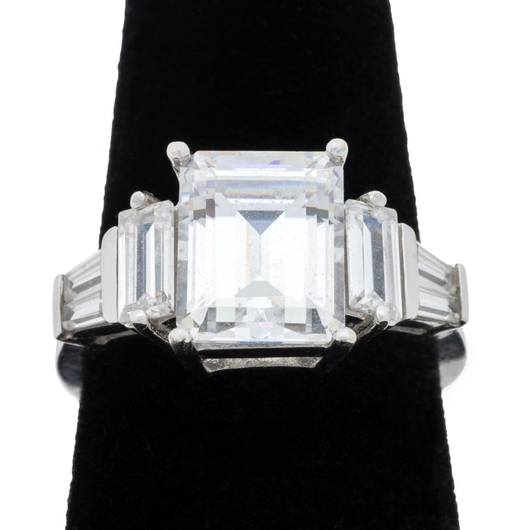 White Gold and Cubic Zirconia Statement Ring: 14K White Gold and Cubic Zirconia Statement Ring, featuring one prong set emerald cut cubic zirconia weighing approx. 6.50 carats, further adorned with six prong set baguette cubic zirconias weighing