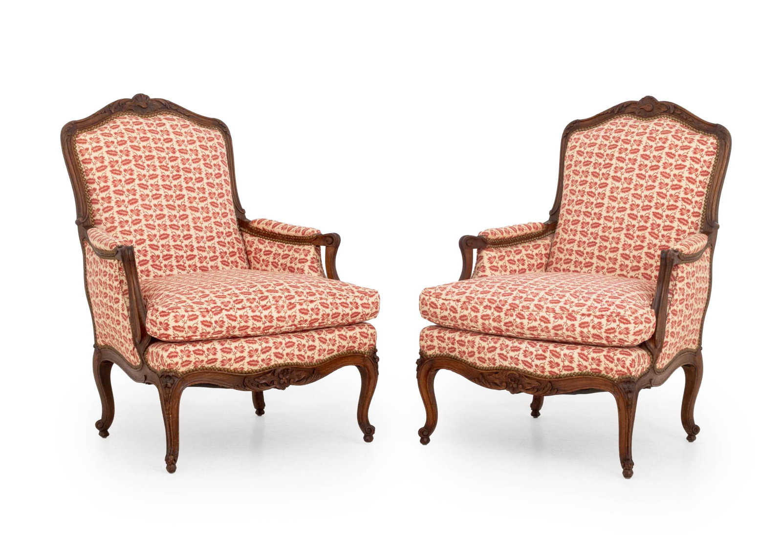 Louis XV Style Upholstered Walnut Bergeres, Pair: Pair of Louis XV Style Re and White Fabric Upholstered Walnut Bergeres, each with carved floral motif cresting and riveted brass nailhead details. 39.5" H x 28" W x 29" D; seat: 18" H. Provenance: An 