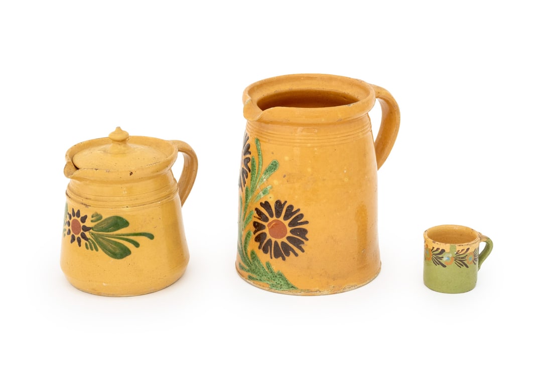 French Alsatian Glazed Pottery Tableware, 3 Pcs.: Group of Three French Alsatian Glazed Pottery Tableware Pieces, comprising: two pitchers in yellow glaze, one with lid, and one teacup in green and yellow glaze. Largest: 8.75" H x 9.25" W x 7.25" D.