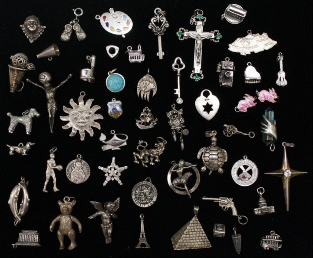 Lot of Assorted Sterling Silver Charms 200 grams: A lot of assorted sterling charms including a teddy bear, the Eiffel tower, a palette board, a pyramid, a robot, a magic lamp, a cuckoo clock, and more. Weight and dimensions: 200 grams, Sizes range 1