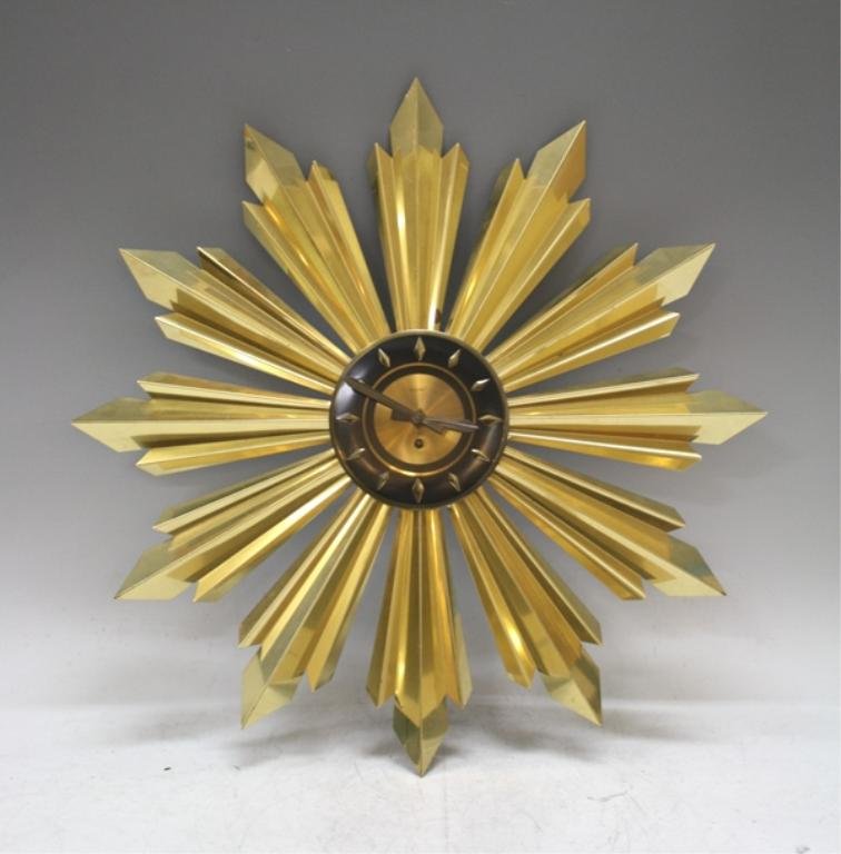 Mid Century Welby Sunburst Clock: A Mid Century metal Sunburst clock with a black and gold colored face. Manufactured by Welby Clock Company, Marked "Welby" "8 Day"; marked. Dimensions: approximately 27" diameter