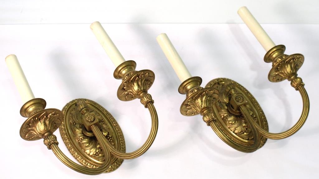 Pair of Neoclassical Fire-Gilt Bronze Sconces: Oval in form, with dual reeded arms extending from a flower- and acorn-festooned square, the surface, drip pans and candle cups embossed with grapes, vine and palmetto leaves, with faux candle forms i
