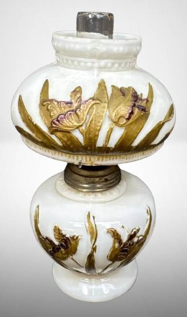 Miniature Milk Glass Lamp with Floral Design: Miniature milk glass lamp featuring embossed floral designs in gold and purple. Includes a clear glass chimney and brass fittings. Base shows an applied circular foot. Overall condition appears consis