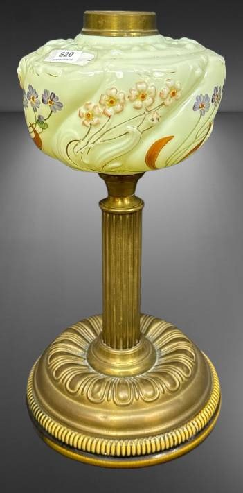 Art Nouveau Style Glass and Brass Lamp: Art Nouveau style lamp featuring a custard-like font with floral handpainted and embossed motifs, mounted on a fluted brass column and base with a ridged design. Notable condition detail includes a ch
