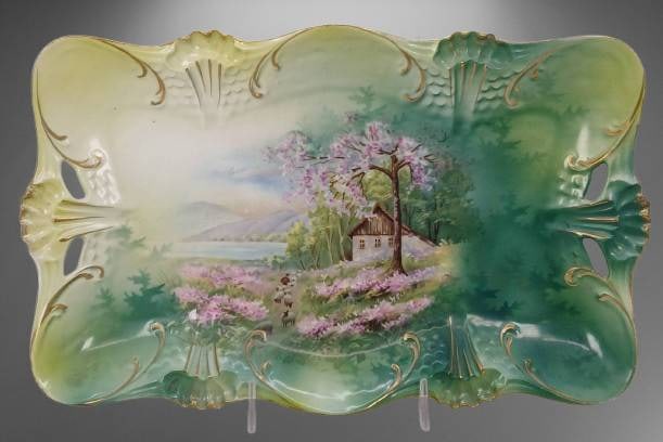 RS Prussia Hand-Painted Rectangular Dresser Tray: RS Prussia porcelain hand-painted rectangular tray featuring a pastoral scene of a cottage and blooming trees. Decorated with embossed detailing, open handles, and gold accents. Measures approximately