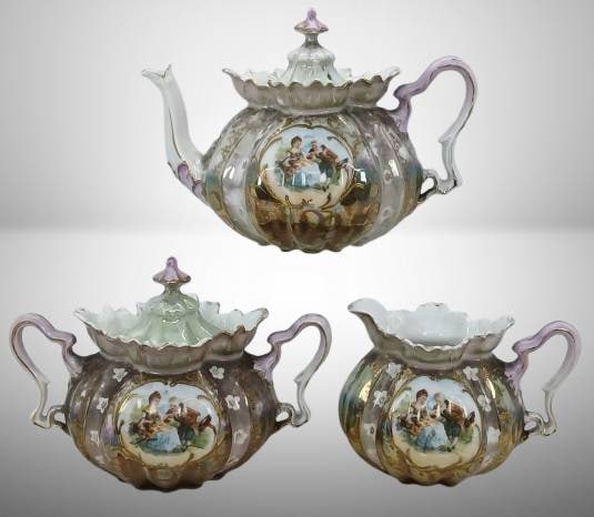 RS Prussia 3-Pc. Tea Set ?: RS Prussia 3-piece tea set includes a teapot, creamer, and sugar bowl with lid. Features ornate floral and figural decorations with gold detailing. ? Overall vibrant luster and detailed design.