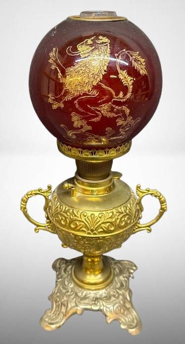 12-Inch Brass Oil Lamp with Etched Glass Globe: Brass oil lamp standing 12 inches tall, featuring ornate detailing and a red etched glass globe with gold lion and decorative motifs. Marked 'Made in United States of America.' Includes a clear glass 