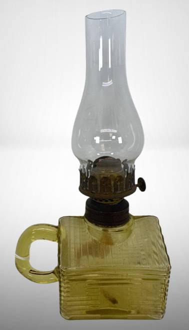 Atterbury Amber Glass Log Cabin Lamp: Atterbury amber glass miniature lamp in the shape of a log cabin, featuring a square base with handle and a detachable clear glass chimney. The metal burner component is intact. Shows minor wear consi