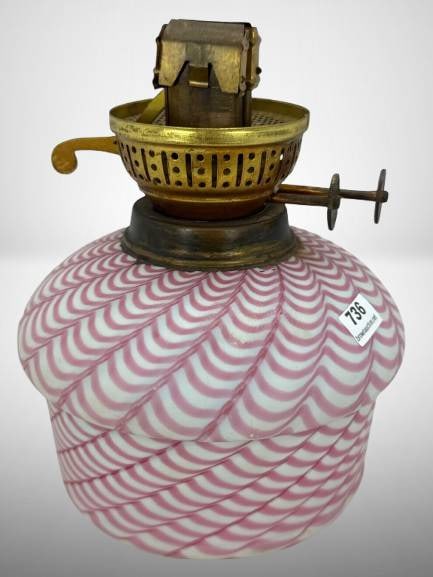 English Duplex Brass and Glass Oil Lamp: An English-made oil lamp featuring a brass duplex burner labeled "Made in England". The base is crafted from opaque whhite glass in a reverse swirling pink and white pattern. Includes turn keys for wi