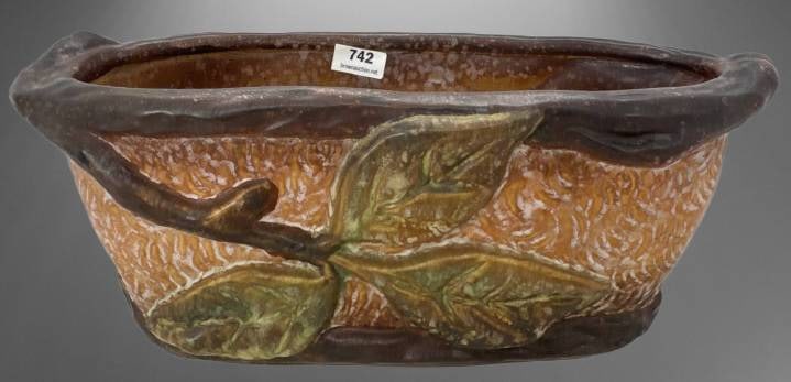 Weller Warwick Oval-Shaped Planter: Weller Warwick oval-shaped planter with a textured ochre-toned body and raised decoration of green leaves on a brown branch motif. Marked 'Weller' on the base. Displays age-related crazing and patina 