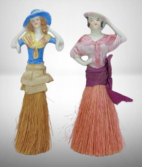 Japanese Bisque Doll Brushes: Bisque doll brushes featuring hand-painted porcelain upper bodies and natural fiber bristles. Marked 'Japan' on the blue doll. Light signs of wear. Measurements visible in image. A charming collectibl