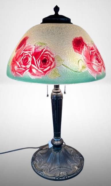 Table Lamp with Reverse Hand-Painted Roses Shade: 21" tall table lamp featuring a reverse-painted glass shade adorned with red rose motifs. The metal base, in bronze-tone, has intricate detailing. Pull-chain light sockets and wiring are visible. Incl