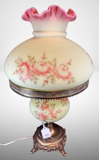 Fenton Burmese Table Lamp with Hand-Painted Roses: Fenton Burmese glass table lamp with hand-painted rose designs, signed by artist. Lamp features a ruffled pink top, a brass-toned metal base, and gilded detailing. Electrified and functional, bulb inc