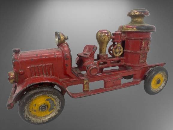 Cast Iron 11" Red Toy Fire Truck: Cast iron toy fire truck measuring 11" long, painted red with yellow wheels and gold detailing. Features intricate design elements, including a boiler and seating area. Shows signs of wear consistent 