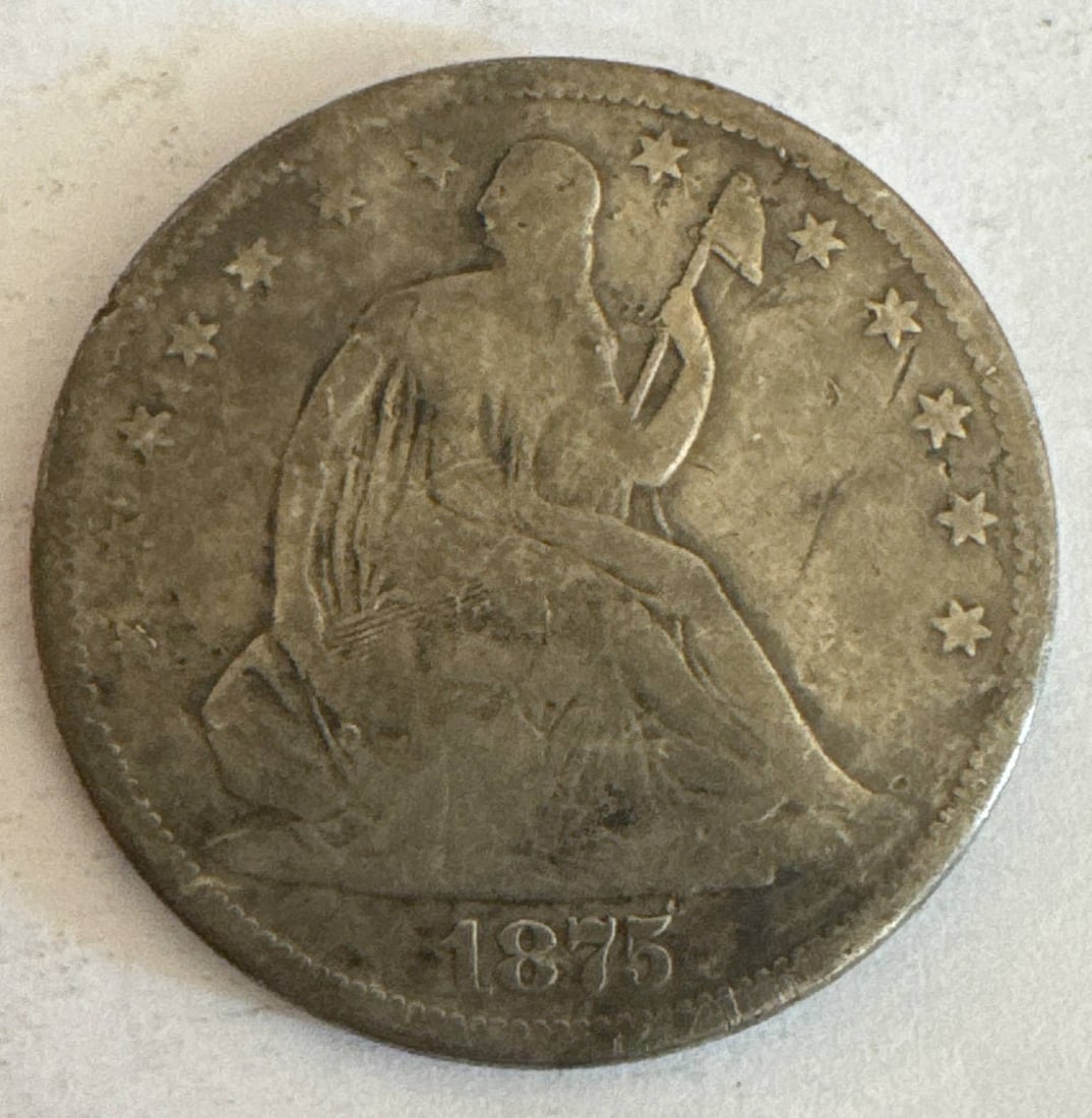 1875-S Seated Liberty Half Dollar: An 1875-S Seated Liberty Half Dollar minted in San Francisco. Made of 90% silver and 10% copper. Highlights Liberty seated on obverse and an eagle on the reverse. Visible wear and toning are present d
