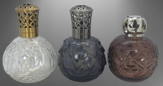 (3) Lampe Berger Paris Lamps: (3) Lampe Berger Paris catalytic fragrance lamps. Includes clear, smoked gray, and amber-tone glass designs with decorative vented caps in gold, silver, and chrome finishes. Stamped ??Made in France'