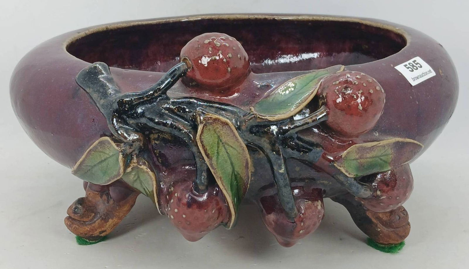 Majolica-Style 3-Footed Ceramic Bowl: Majolica-style 3-footed bowl featuring an embossed fruit and branch motif against a deep burgundy glaze. Minor surface wear noted with no chips, cracks, or repairs. Marked on the underside. Measures 9