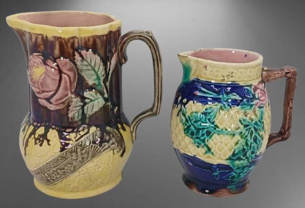 (2) Majolica-Style Ceramic Pitchers: (2) Majolica-style pitchers, 5" and 6". Each features floral relief designs and vibrant glazes. Signs of wear evident, including cracks and chips as shown in photographs. Makers' marks visible on tall
