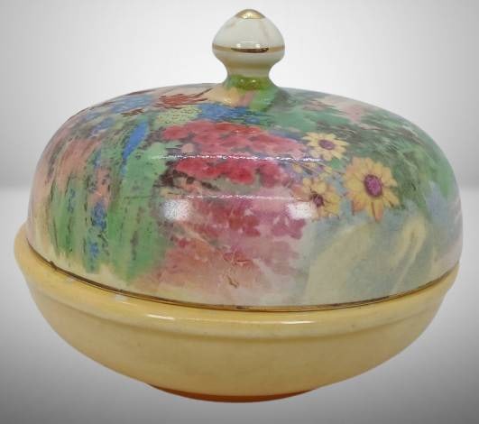 Crown Ducal Lidded Powder Jar: Crown Ducal lidded powder jar featuring a floral chintz design on the lid and a soft yellow base with gold detailing. Marked 'Crown Ducal Made in England' on the underside. Includes a visible chip on