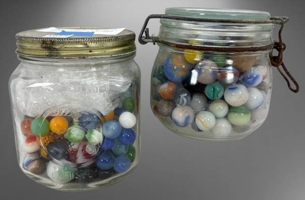 Two Jars Containing Assorted Marbles: Marbles housed in two glass jars, including large "shooters" and standard-size marbles of various colors and patterns. Jars feature metal and glass lids with rust present on closures. In-house shippin