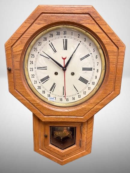 Oak Wall Regulator Clock With Brass Pendulum: This oak-case wall clock features Roman numerals, a 31-day calendar, and brass pendulum. Its octagonal shape is distinct, and the interior mechanism is intact and visible through the lower door. A cla