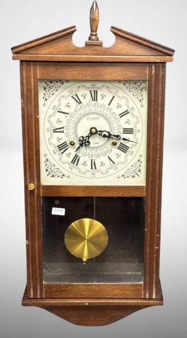 24-Inch Wooden Case Wall Clock by L. Gant: Standing 24 inches tall, this wooden case wall clock by L. Gant features a decorative Roman numeral dial, brass pendulum, and intricate interior mechanism. The hinged glass door opens to reveal the fa
