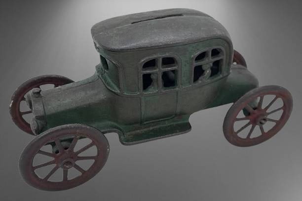 Cast Iron Automobile Coin Bank: This cast iron coin bank, shaped like an early 20th-century automobile, is likely crafted by A.C. Williams. It features detailed window cutouts and four large spoked wheels that spin freely. A slot on