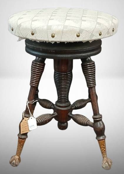 Adjustable Piano Stool With Claw Feet: This wooden piano stool features intricately turned legs, accented with notable cast metal claw and ball feet. The seat is upholstered with vintage-style fabric and sits atop an adjustable mechanism f