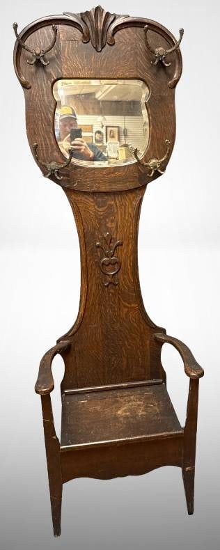 Late 1800s Oak Hall Tree With Beveled Mirror: This late 1800s oak hall tree features a beveled mirror and ornate cast iron coat and hat hooks. Crafted from solid oak, it includes integrated seating with a lift-up storage compartment. Measuring 29