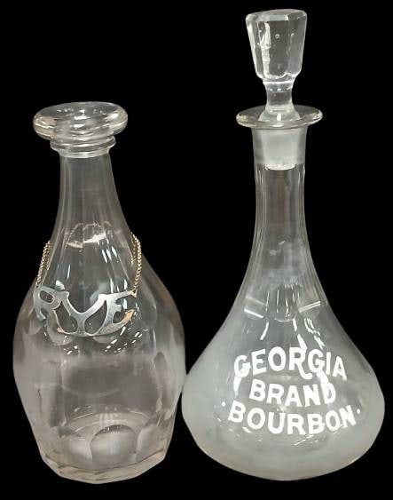 Rye and Georgia Bourbon Decanters: This lot includes two glass liquor decanters: one marked 'Rye' with a metal tag on a chain, and another etched with 'Georgia Brand Bourbon.' Note the bottle stopper for the Georgia Bourbon decanter ha