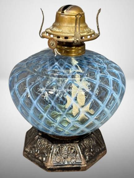 Blue Opalescent Glass Oil Lamp with Cast Iron Base: This oil lamp features a blue opalescent body with a lattice-like diamond patternh functional wick assembly marked as "oQueen Annje No. 2."It is paired with an ornate cast iron base, adding to its cra