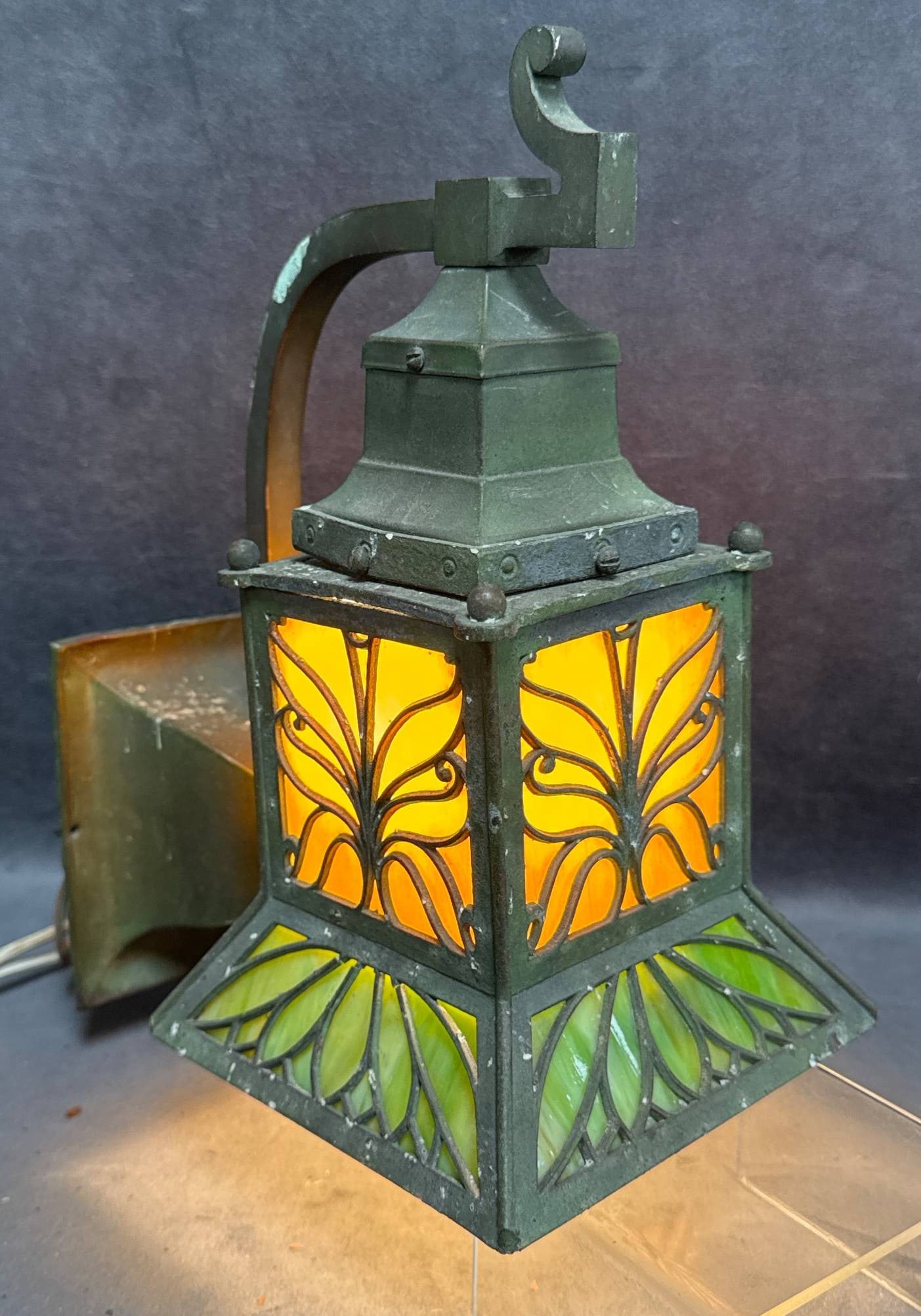 Bradley and Hubbard Slag Glass Wall Sconce: This Bradley and Hubbard slag glass wall sconce features intricately designed panels with amber and green-colored glass set within a metal frame. The sconce is functional but requires rewiring. B&H ha