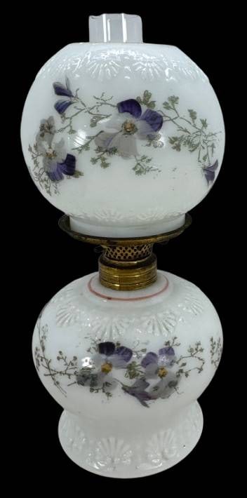 Miniature Lamp With Floral Motifs: This miniature oil lamp features a floral glass shade and base with purple and white flower motifs, complemented by a decorative brass burner. The shade has a base rim chip, as shown. A wonderful addi