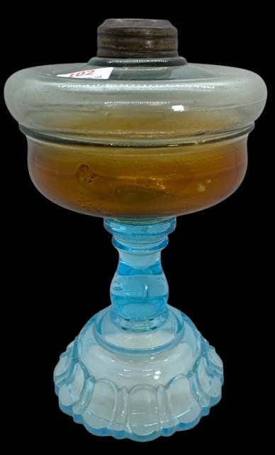 Glass Oil Lamp With Amber and Blue Components: This glass oil lamp features a striking combination of amber and blue glass, with a metal fitting on its reservoir. The base exhibits a scalloped edge design and stands 7.5"h. No chips, cracks, or rep