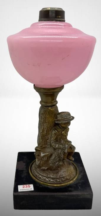Pink Glass Oil Lamp with Boy and Dog Base: This lamp features a pink glass shade paired with a sculpted metal base depicting a boy with a dog. The base rests on a square foundation, providing stability and charm. There are no chips, cracks, or
