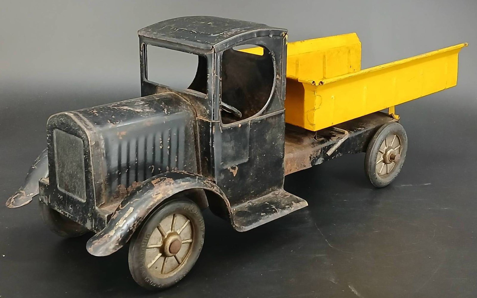Arrow Mfg Co. Toy Dump Truck: Vintage tinplate toy truck by Arrow Mfg Co., Cleveland, Ohio. Features a black cab and yellow dump bed with a functioning lift mechanism. Condition shows wear, rust, and paint loss consistent with age