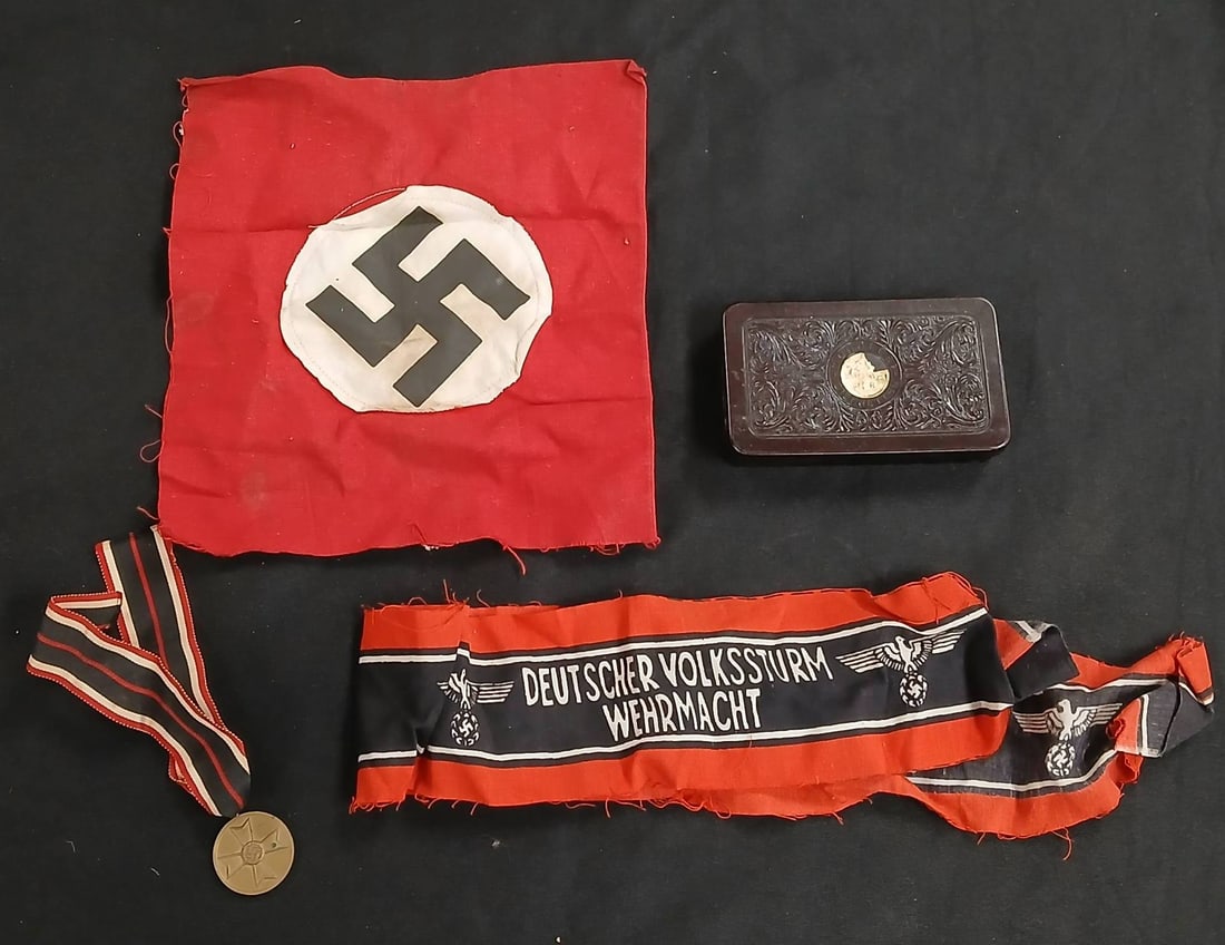 WWII German Military Memorabilia Assortment: Collection includes a Deutscher Volkssturm Wehrmacht armband, a Swastika flag fragment, a medal with ribbon, and a decorative cigarette case. Items display wear consistent with age. Sold for historica